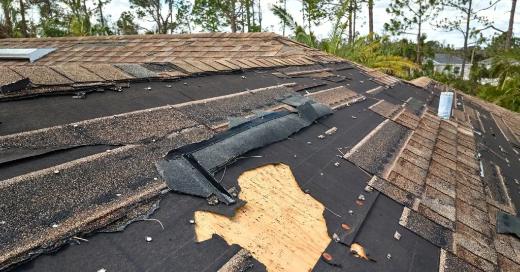 Severely damaged residential roof with torn asphalt shingles, exposed underlayment, and wooden decking.
